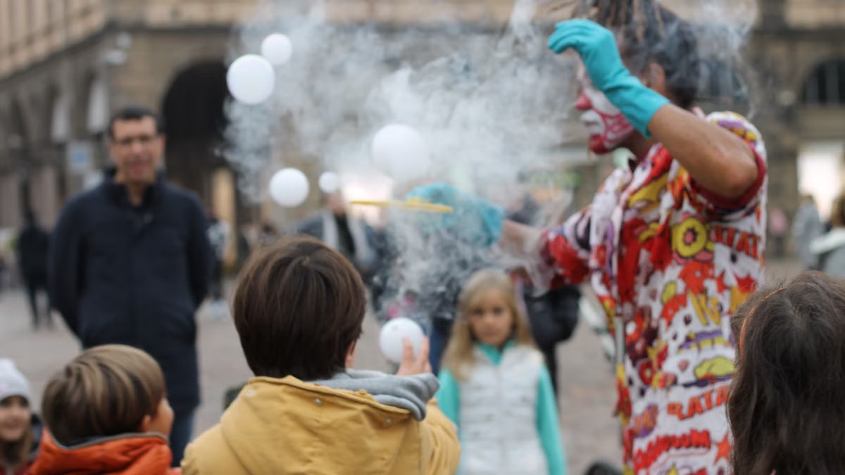Playful clown entertains kids with magic tricks and bubbles in a lively urban setting.